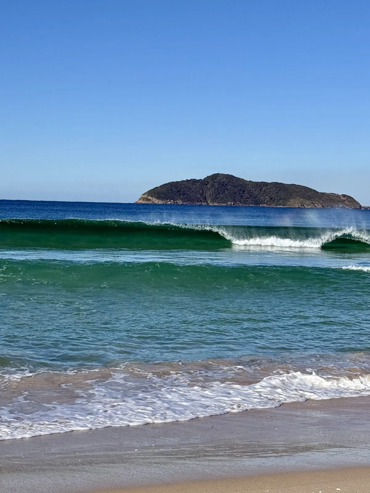 Emerald green wave breaking at Bennetts Beach with Broughton Island beyond