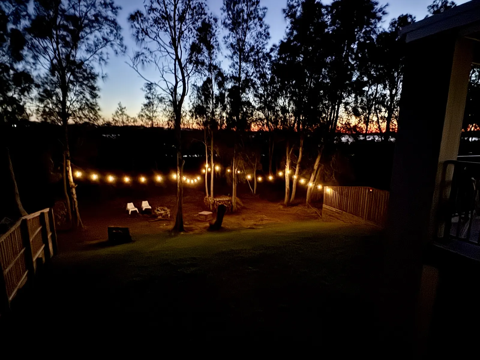 Fire pit and festoon lights at dusk in the garden at Drift, Tea Gardens, with sunset over the Myall River